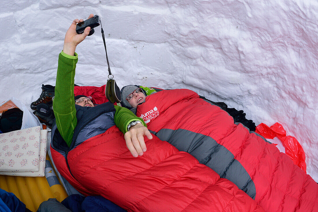 Zwei Personen liegen in Iglu und fotografieren Selfie, Chiemgauer Alpen, Chiemgau, Oberbayern, Bayern, Deutschland