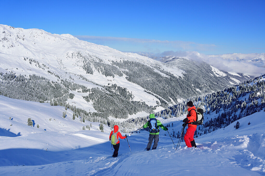 Three persons back-country skiing downhill from Pallspitze, Pallspitze, Langer Grund, Kitzbuehel range, Tyrol, Austria