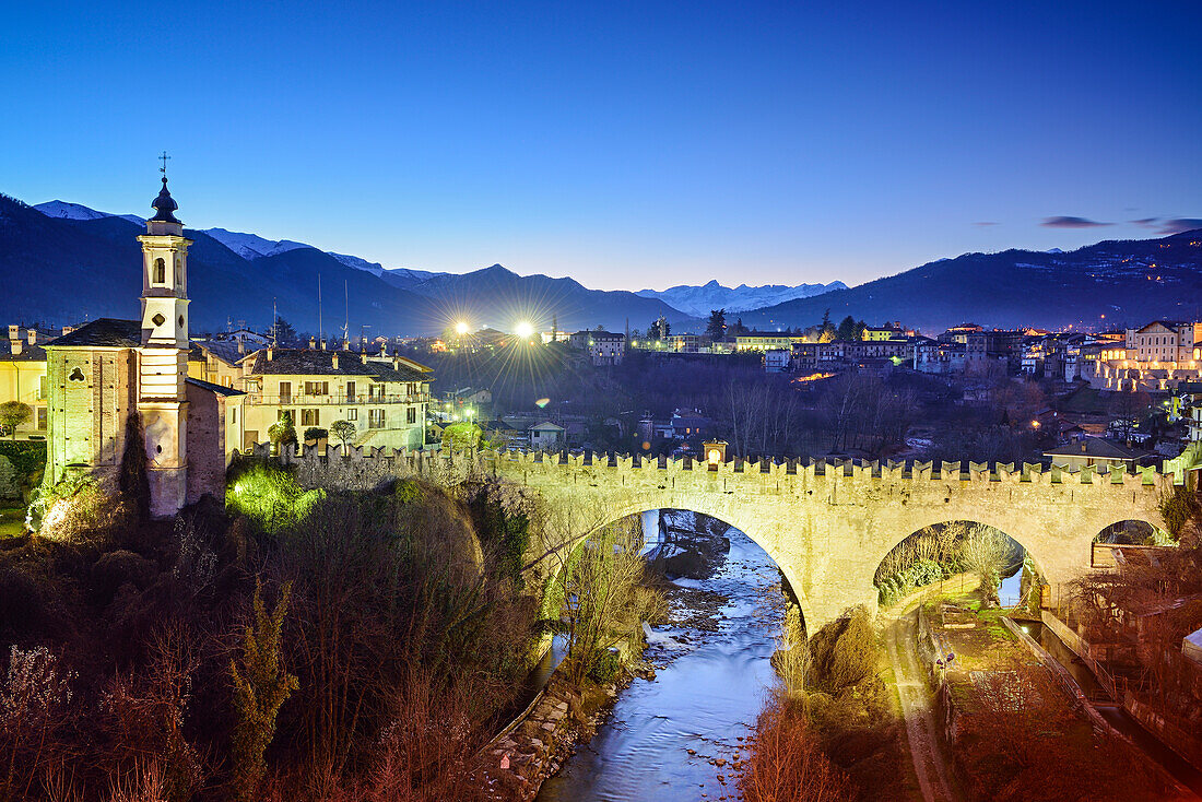 Illuminated village of Dronero with Ponte del Diavolo and river Maira, Dronero, Valle Maira, Cottian Alps, Piedmont, Italy