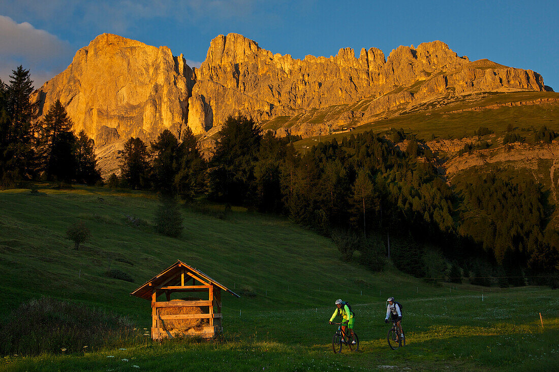 two mountain bikers at sunset in front of Latemar, Trentino Italy