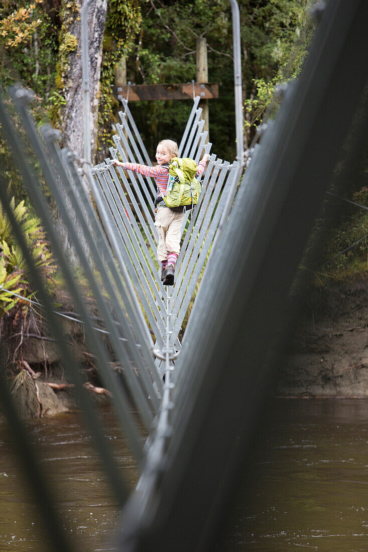 Ein Mädchen überquert eine Drahtseilbrücke beim Lake Manapouri, Südinsel, Neuseeland