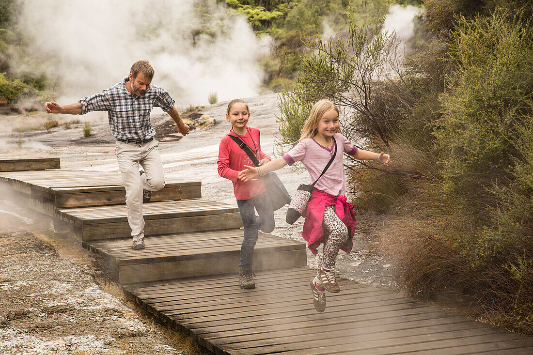 Father with his two children running down steps, Sinter terraces at Orakei Korako (Hidden Valley) geothermal area, Taupo Volcanic Zone, North Island, New Zealand
