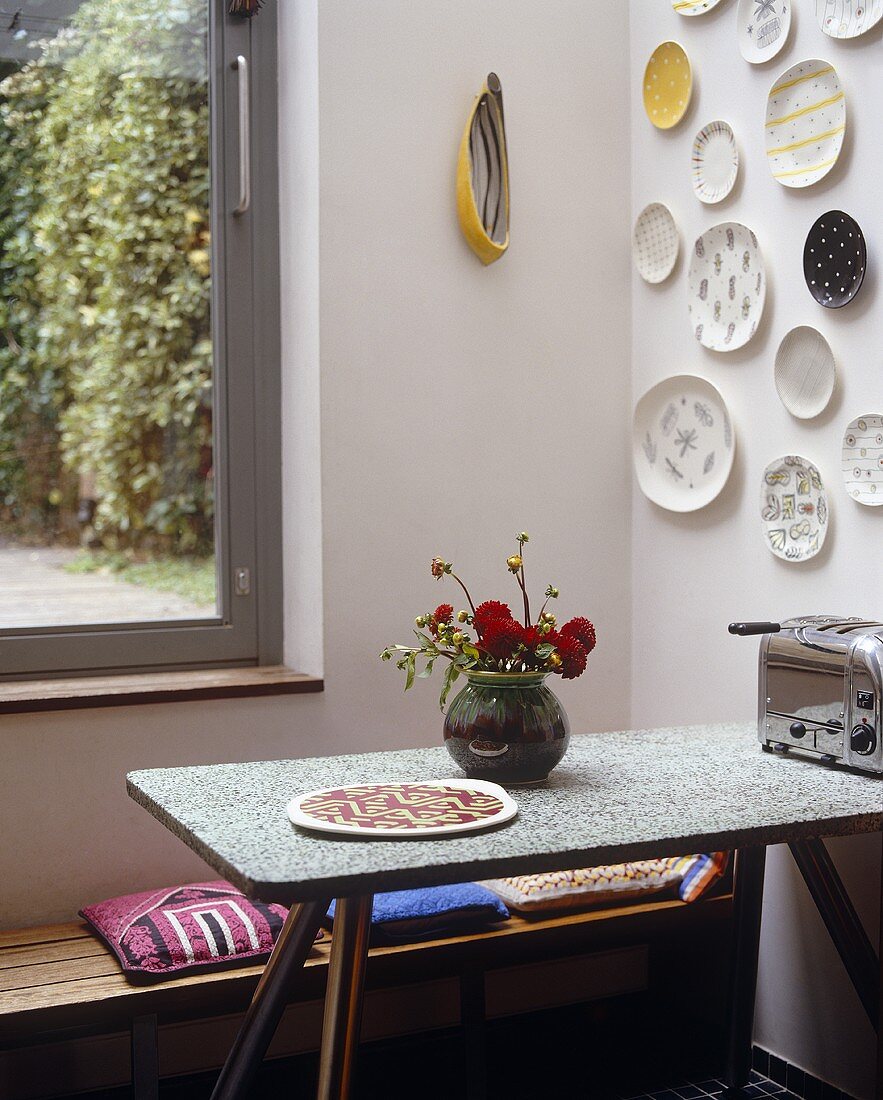 A corner of a kitchen with plates hanging on the wall above a table and a bench