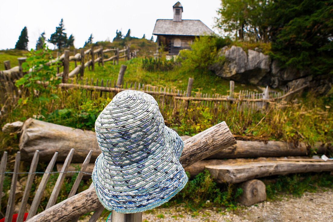 Sun hat hanging on a fence in front of the Herz-Jesu-Kapelle at Stiealm, Brauneck, Lenggries, Alps, Bavaria, Germany