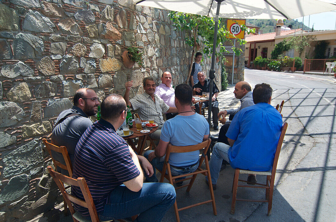 Men sitting at bar tables along the road in Gourri village about 30km westl of Lefkosia, Nicosia, Cyprus