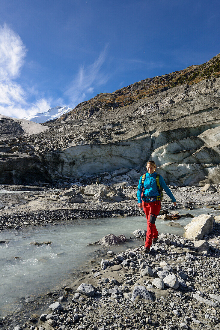 Woman crossing the Morteratsch Creek near the glacier mouth of Morteratsch glacier with view to Piz Bernina (4049 m), Engadin, Grisons, Switzerland