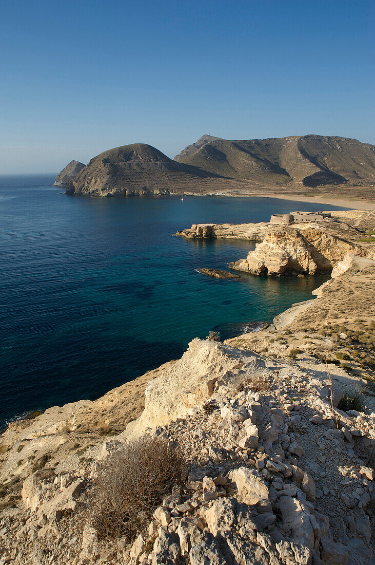 Blick von einem Hügel über die felsige Küste und eine Festung am Cabo de Gata in der Provinz Almeria, Andalusien, Spanien