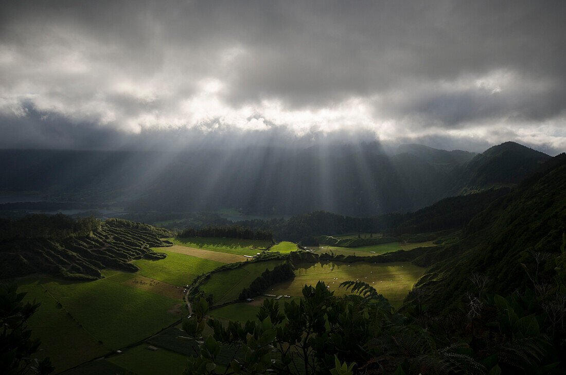 The sun breaking through the clouds and shining on green meadows, in the background the crater called Sete Cidades with the lakes Lagoa Azul and Lagoa Verde, Island of Sao Miguel, Azores