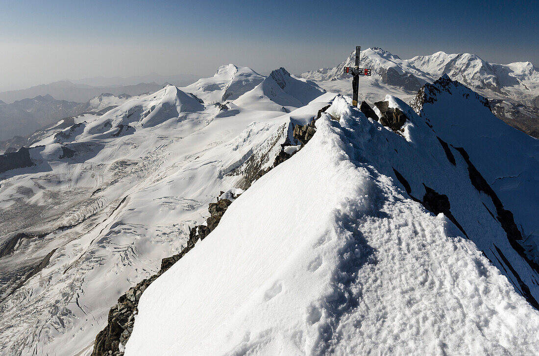 The summit cross of Dom, highest peak entirely on Swiss ground, behind the massif of Monte Rosa, Pennine Alps, canton of Valais, Switzerland