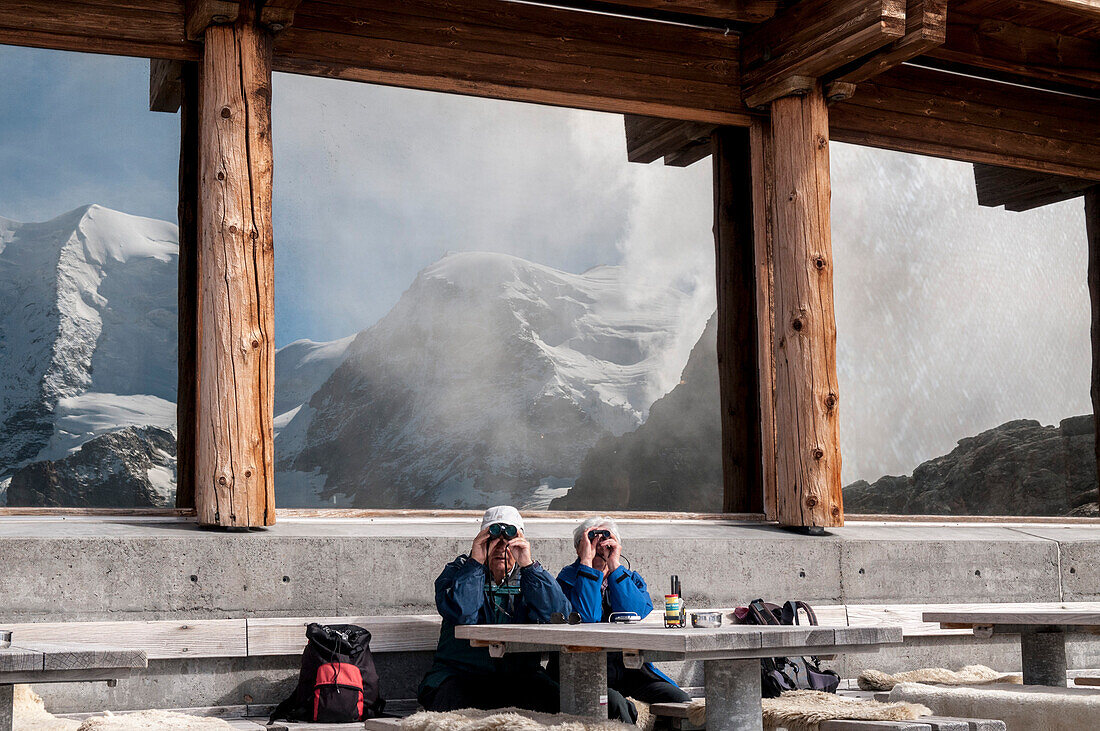 An elderly couple sitting on the terrace of the Mountain Hut Diavolezza and looking towards the mountains around Piz Palue, Grison Alps, canton of Grison, Switzerland