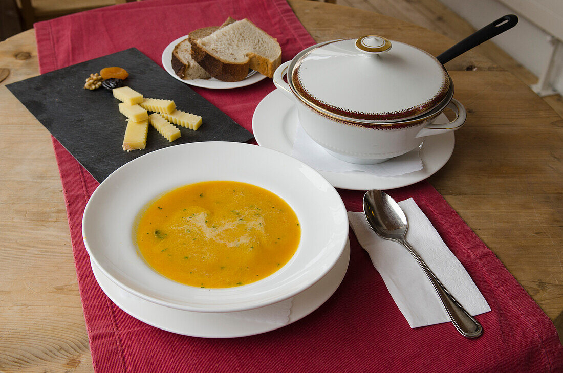 Eine antike Suppenschüssel, ein Suppenteller mit Kürbissuppe und ein Käseplättchen im Hotel Ofenhorn in Binn, Kanton Wallis, Schweiz