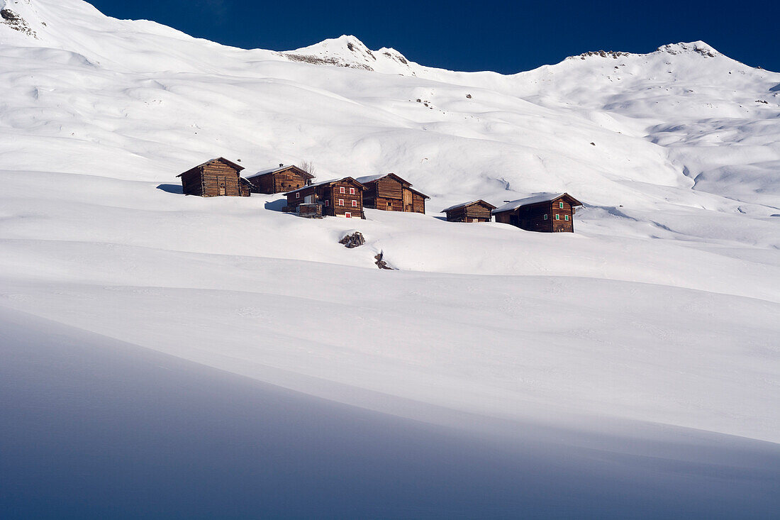 Die Holzhäuser des Weilers Meierhof mitten in der tief verschneiten Landschaft des Hochtals namens Fondei, Bündner Alpen, Kanton Graubünden, Schweiz