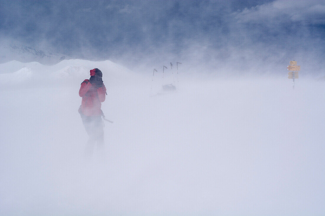 A backcountry skier with a DSLR camera taking a picture in a storm caused by Foehn winds, summit of the Mattjisch Horn, high valley called Fondei, Grison Alps, canton of Grison, Switzerland