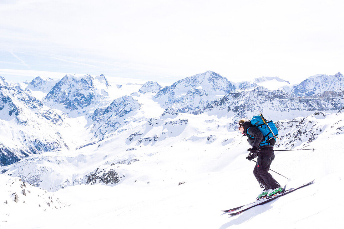 A young female backcountry skiing, skiing downhill from the summit of Mont de l‘Etoile towards the Aiguilles Rouges Hut, behind from left to right the summits of Mont Collon, Pigne d‘Arolla and Mont Blanc de Cheilon, Val d‘Hérens, Pennine Alps, canton of 