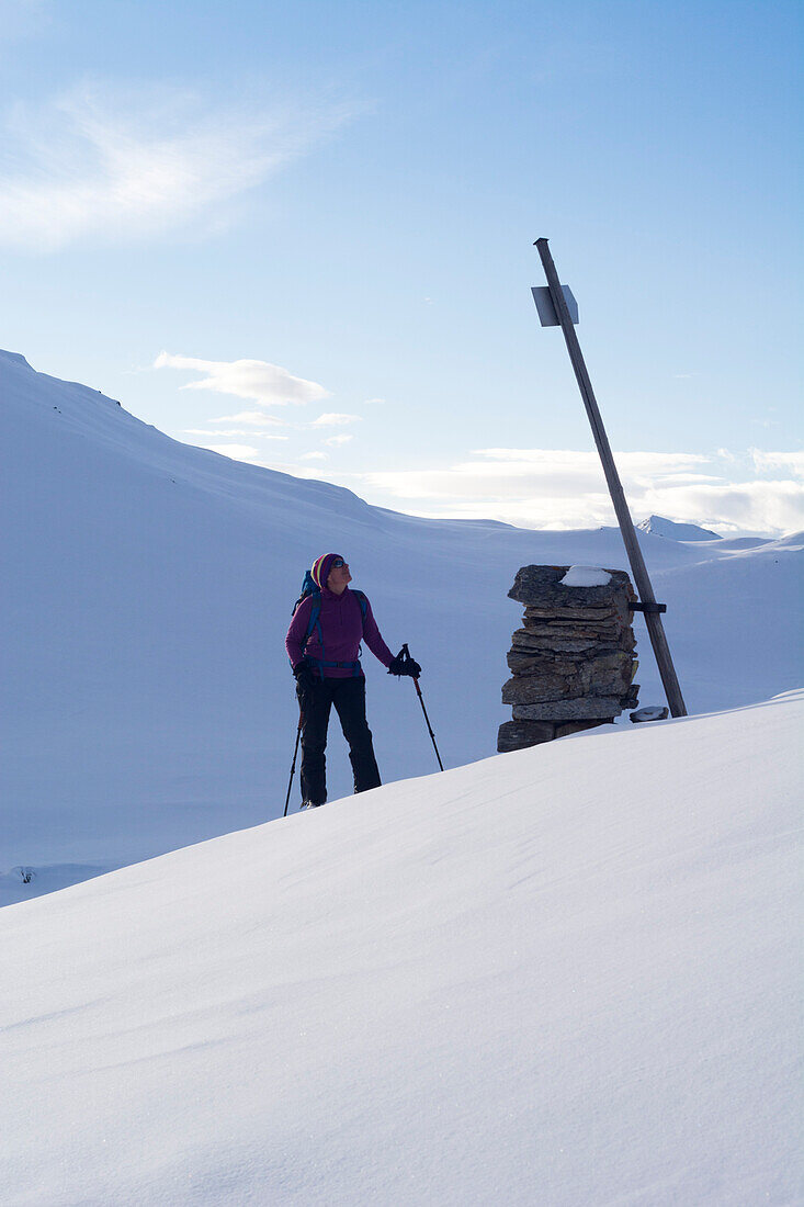 Eine Skitourengängerin betrachtet einen Wegweiser im verschneiten Val Camadra, Lepontinische Alpen, Kanton Tessin, Schweiz