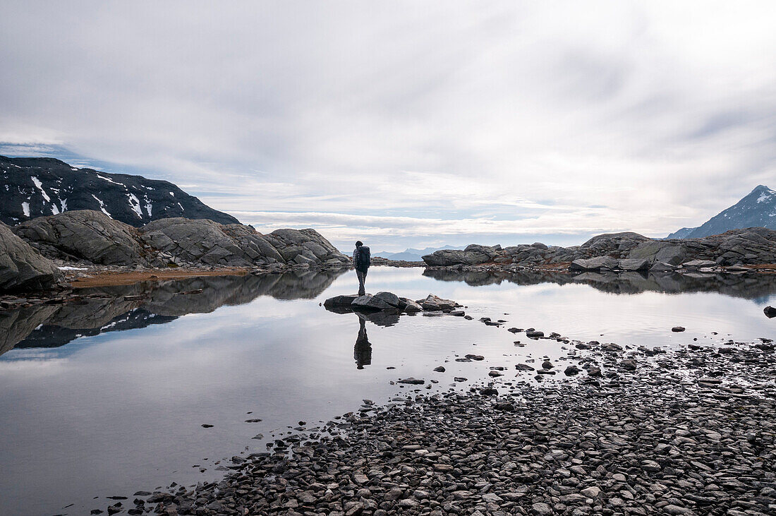 A hiker standing on a stone in a nameless mountain lake near the high plateau of the Greina, Lepontine Alps, canton of Ticino, Switzerland