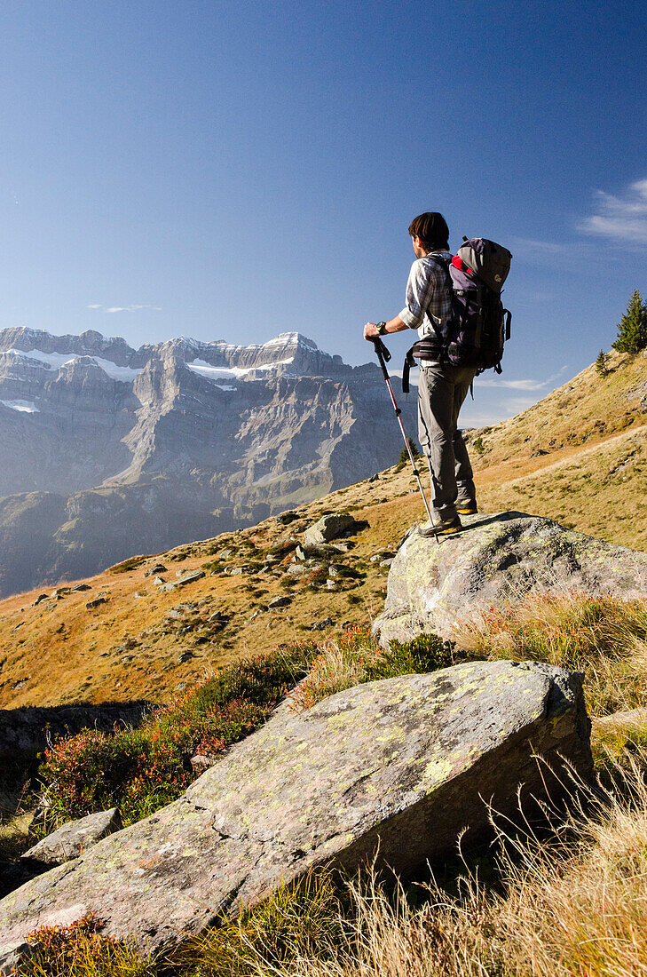 Ein jüngerer Wanderer steht in der Nähe der Mettmenalp auf einem Stein und betrachtet die Gipfel des Glärnisch Massivs, Glarner Alpen, Kanton Glarus, Schweiz