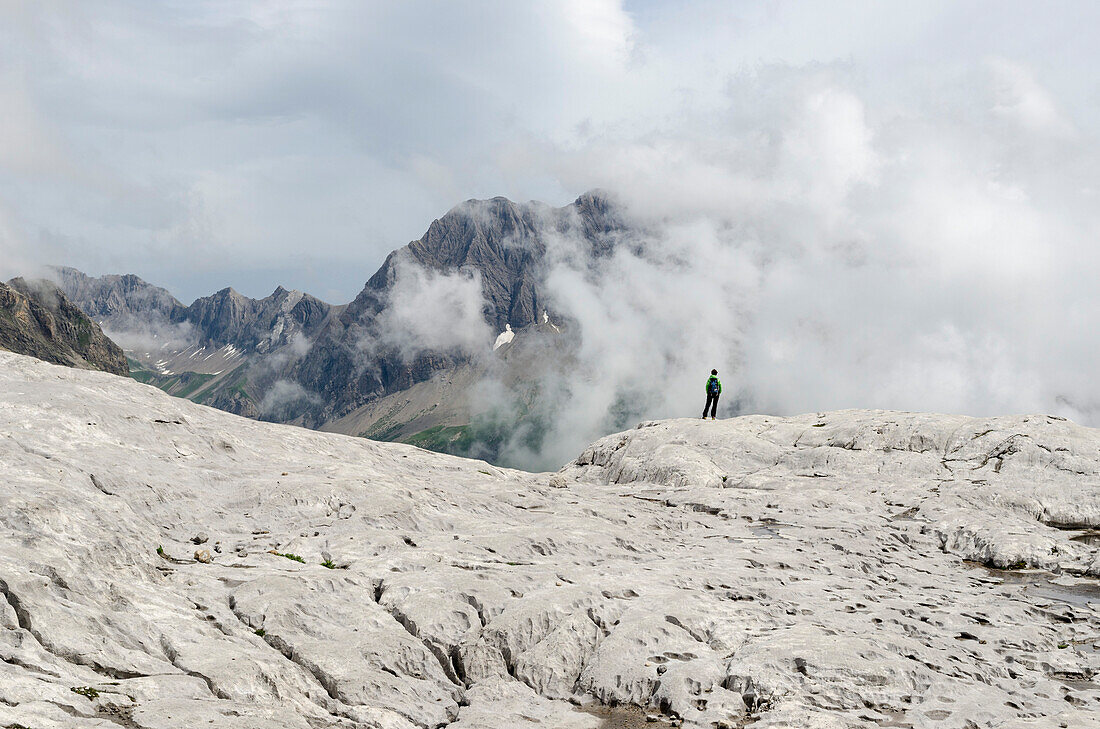 Eine Frau in Wanderausrüstung steht auf einem Karstfeld und blickt auf Gipfel und Wolken, Sanetschpass respektive Col du Sanetsch, Berner Alpen, Kanton Wallis, Schweiz