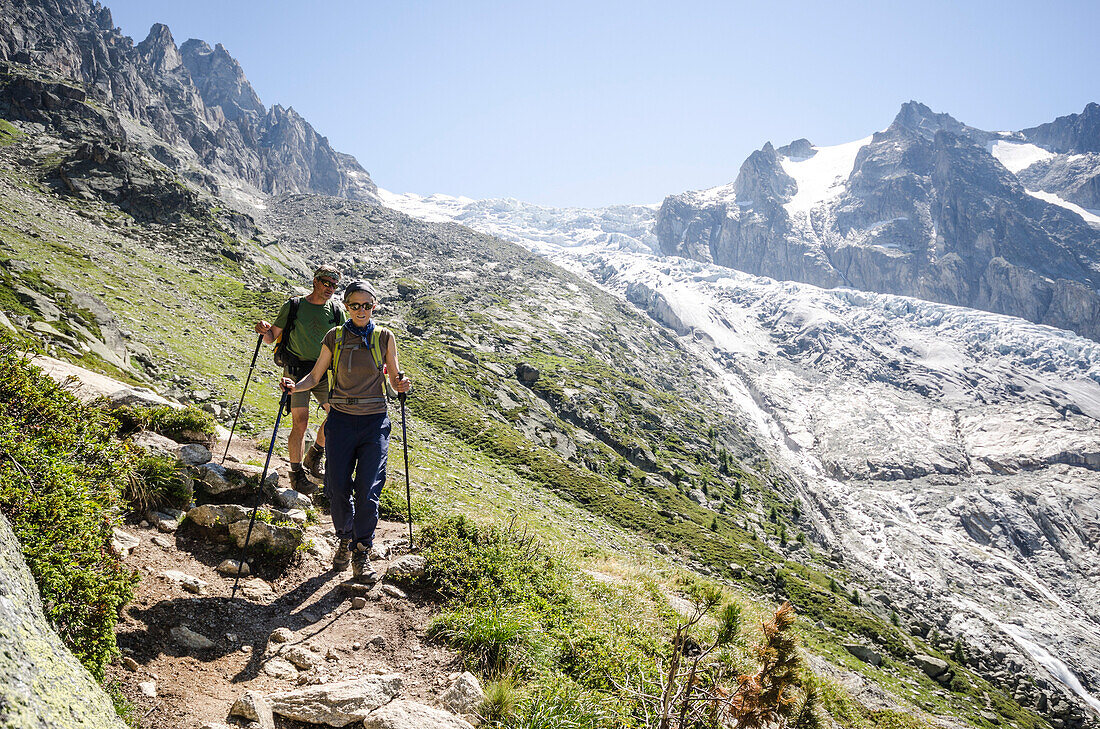A female and a male hiker on a hiking trail descending from the pass Fenetre d'Arpette to the village of Trient, behind them the Trient Glacier, Pennine Alps, canton of Valais, Switzerland