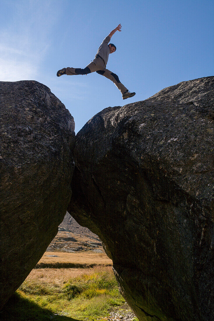 A young man jumping from one boulder to another, Triftji above Zermatt, Pennine Alps, canton of Valais, Switzerland