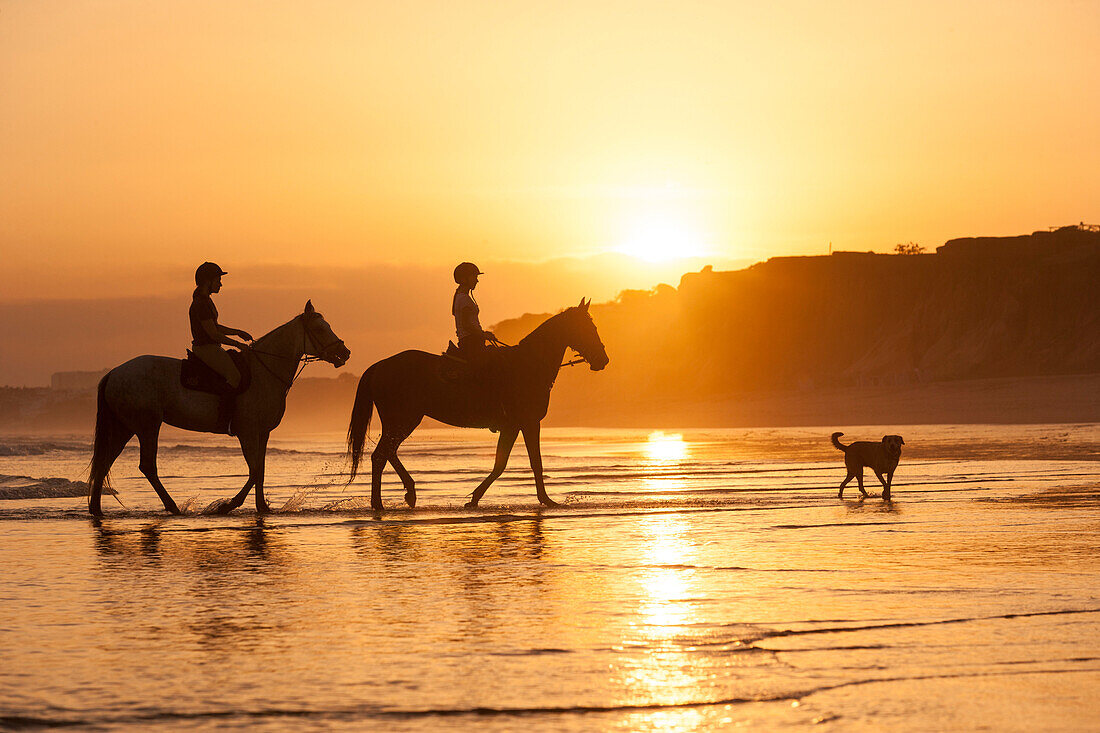 Two young women horse-riding along beach, Algarve, Portugal