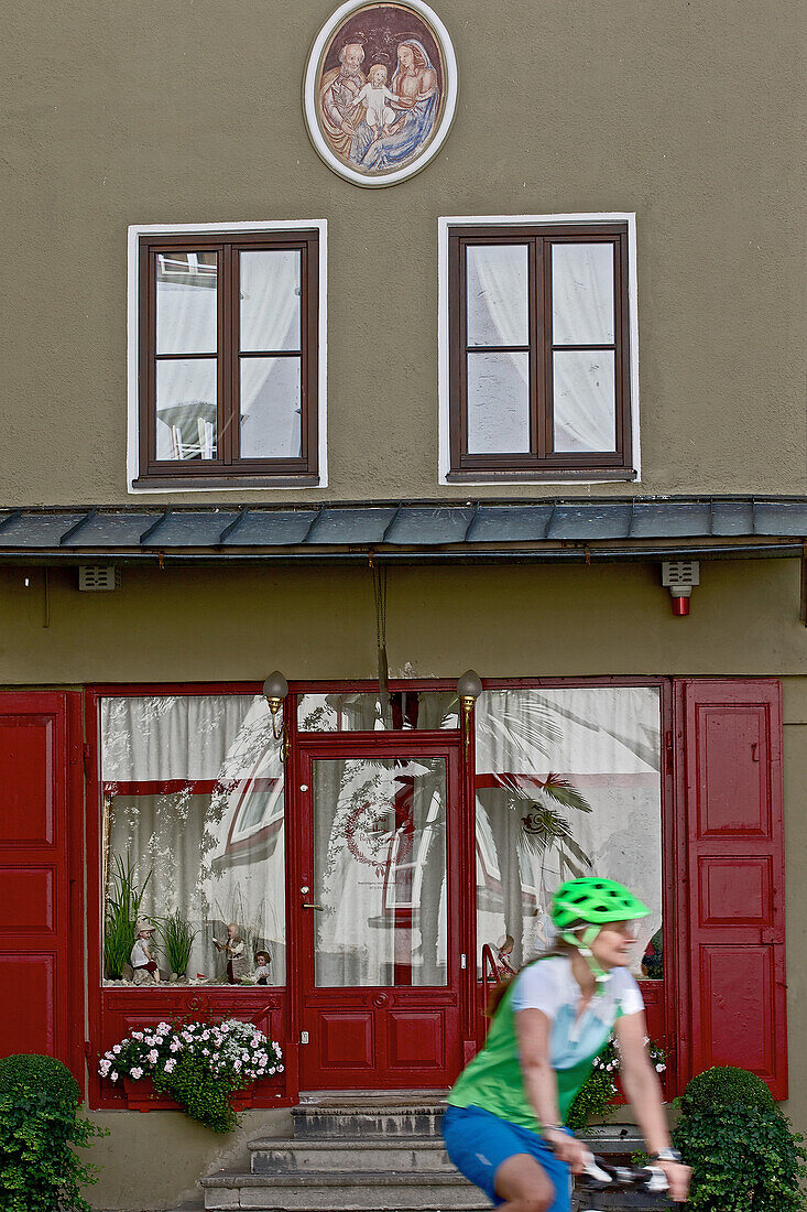 Female cyclist passing a house with a red door, Burghausen, Chiemgau, Bavaria, Germany