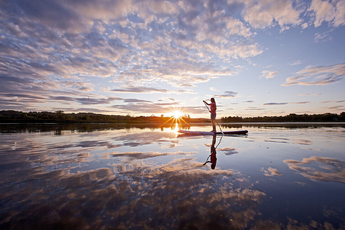 Woman stand up paddling on lake Chiemsee in sunset, Chiemgau, Bavaria, Germany