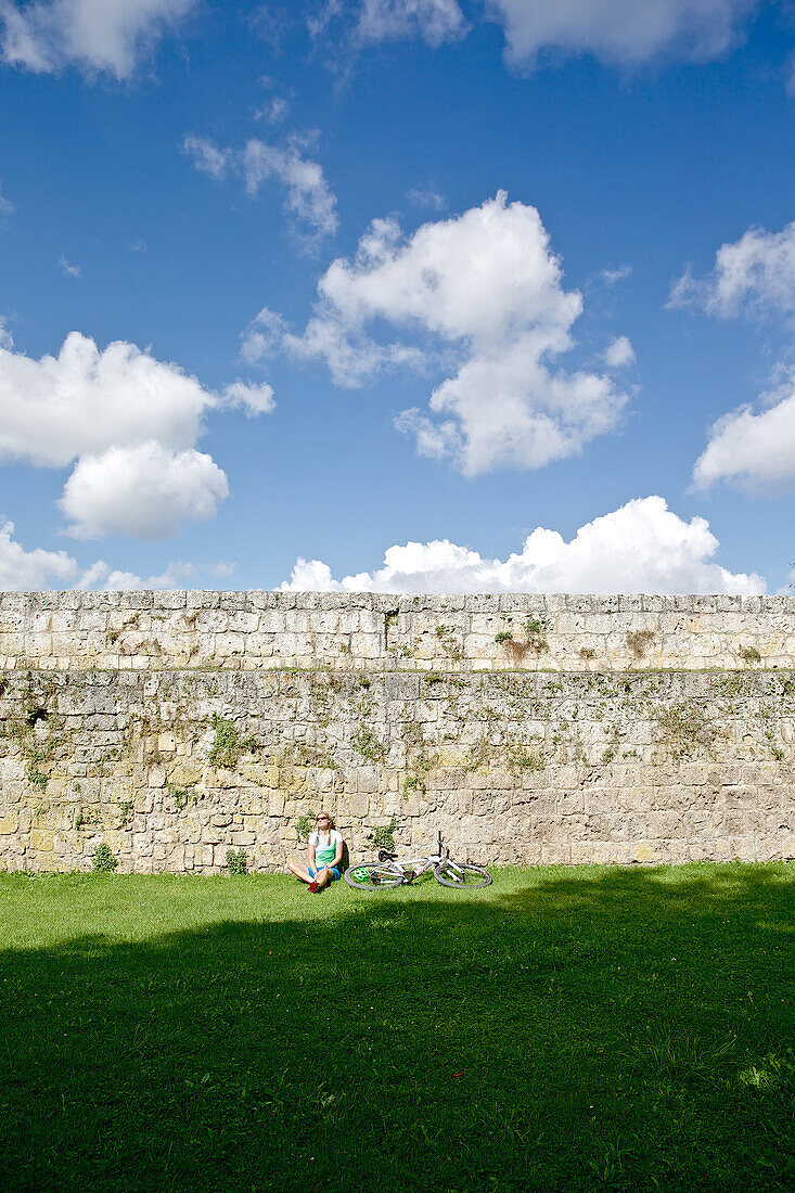 Fahrradfahrerin macht eine Pause an einer Burgmauer, Burghausen, Chiemgau, Bayern, Deutschland