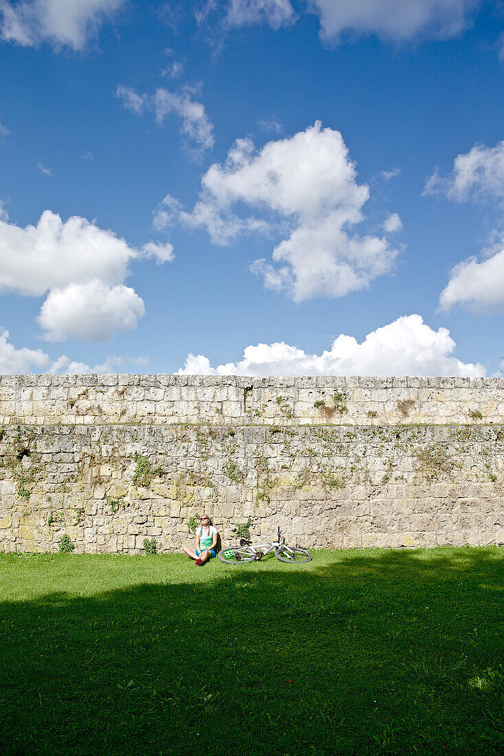 Female cyclist resting at castle wall, Burghausen, Chiemgau, Bavaria, Germany