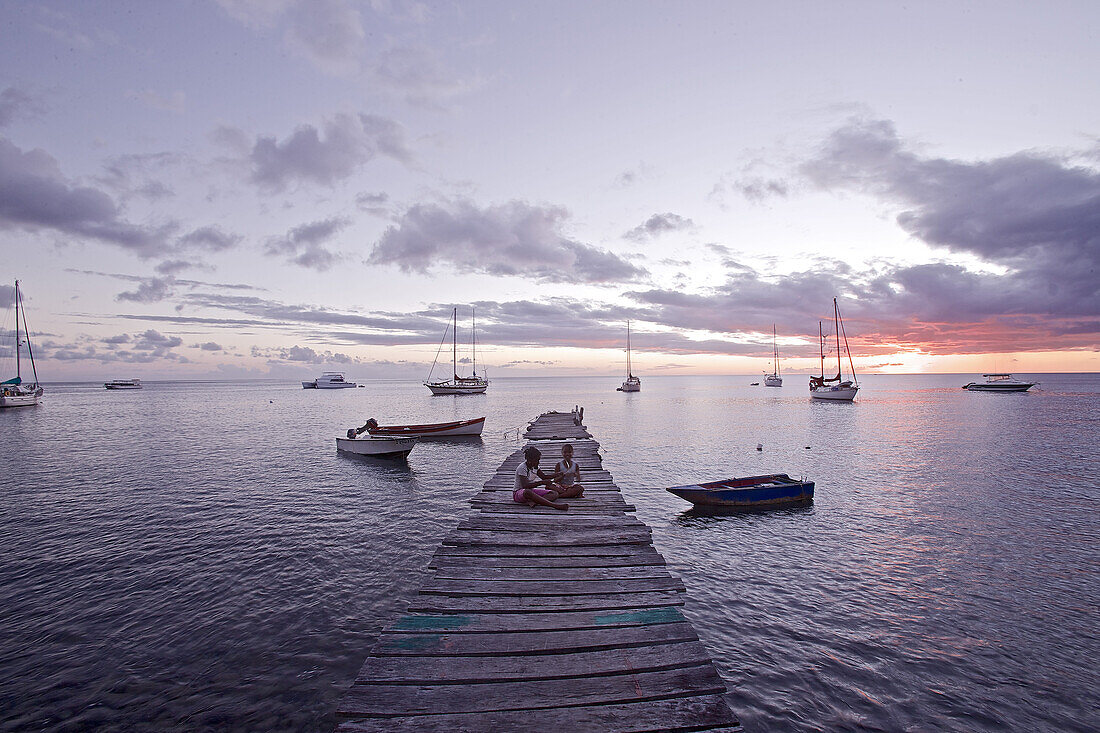 Children sitting on a wooden jetty at the sea in sunset, Dominica, Lesser Antilles, Caribbean