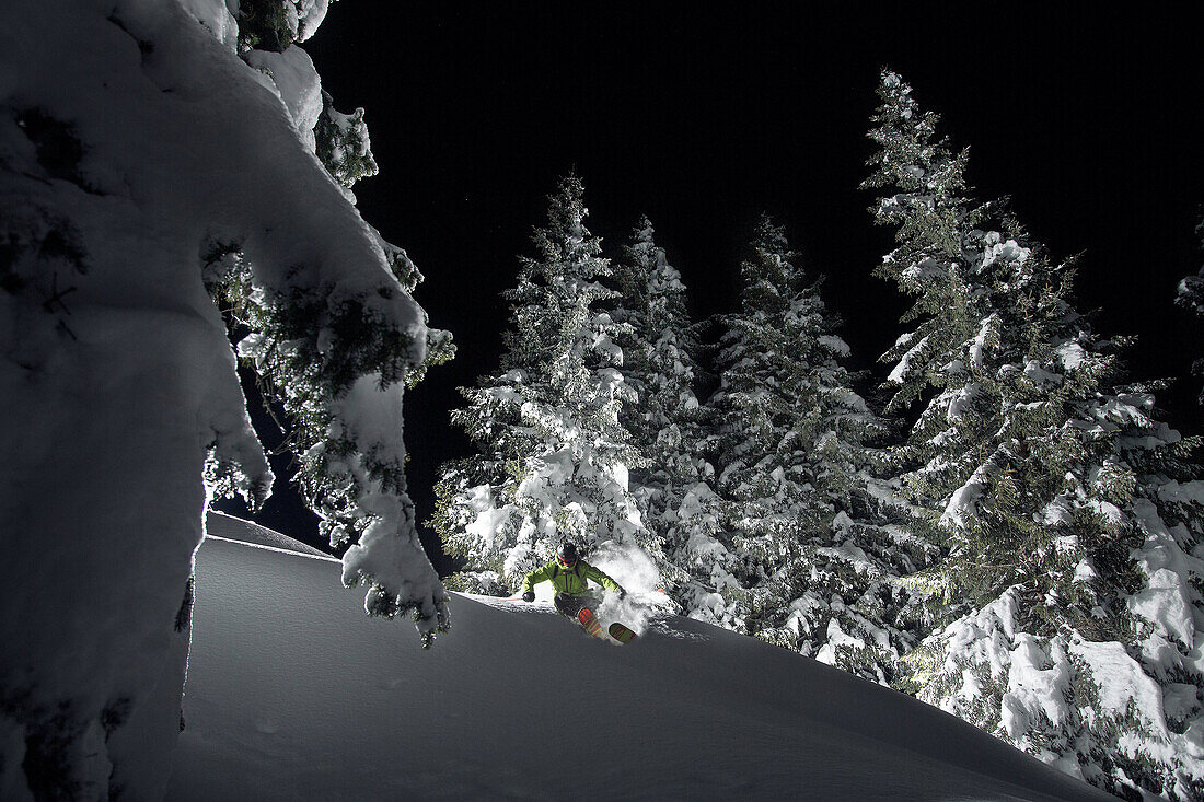 Male freeskier skiing through deep powder snow between trees at night, Stuiben, Bavaria, Germany