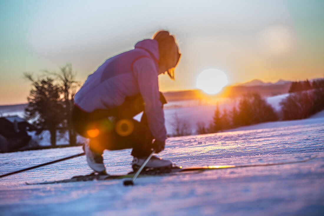 Young woman tying her shoes before cross-country skiing at sunset, Allgaeu, Bavaria, Germany