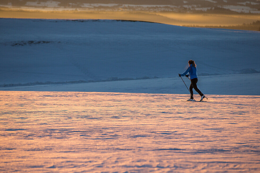 Junge Frau geht Langlaufen während eines Sonnenuntergangs, Allgäu, Bayern, Deutschland