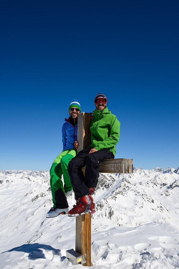 Zwei Männer sitzen auf dem Gipfelkreuz des Schwarzhorns (3147 m), Graubünden, Schweiz, Europa