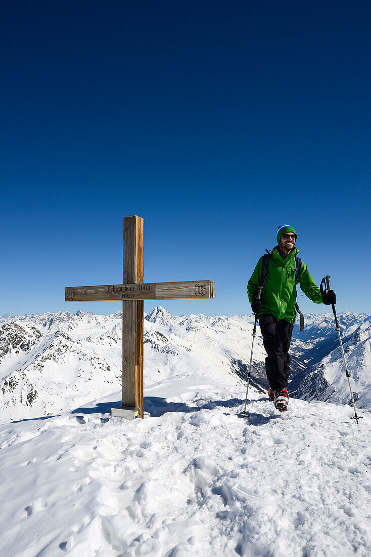 Mann am Gipfelkreuz des Schwarzhorns (3147 m), in der Bildmitte im Hintergrund Piz Linard (3410 m), Graubünden, Schweiz, Europa