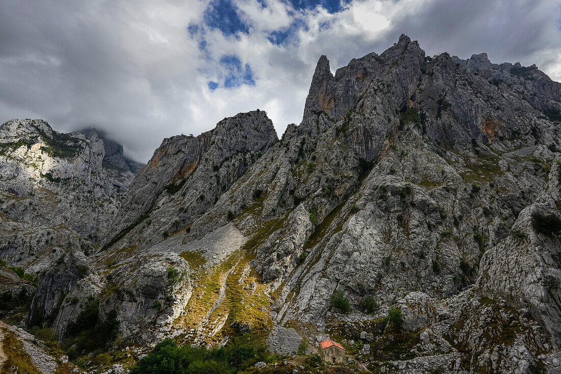 Blick von Camarmeña auf traditionelles Steinhaus eingebettet in schroffe Berge, Cabrales, Gebirge Parque Nacional de los Picos de Europa, Asturien, Asturias, Spanien