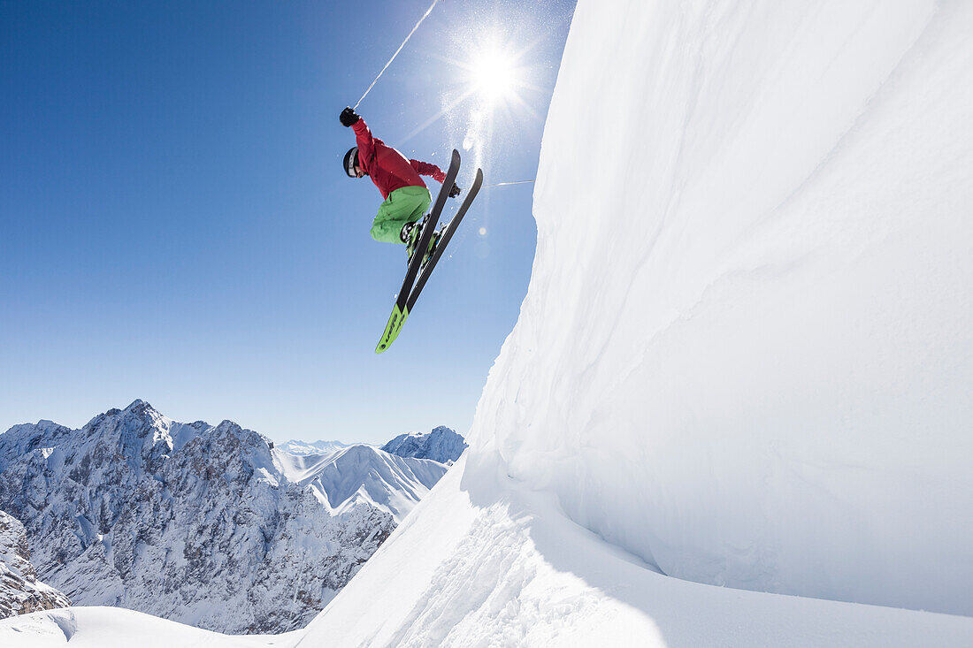 freeride skier jumps over snow cornice, Zugspitze, Hochwanner and Gatterl in the background, Upper Bavaria, Germany