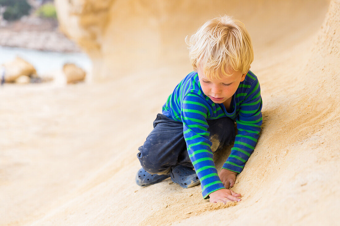 4 year old boy playing with sand on the beach of Portals Vells, MR, near Magaluf, Majorca, Balearic Islands, Spain, Europe