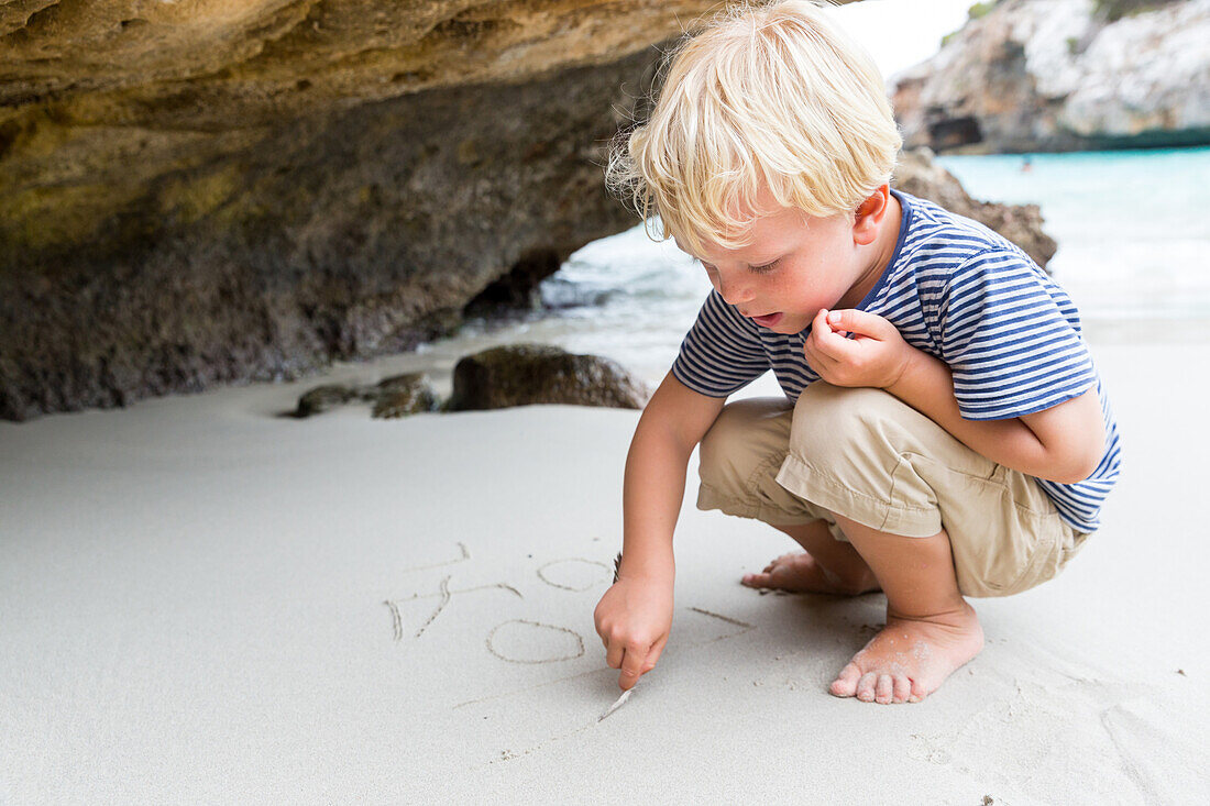 Junge schreibt in den Sand, Strand bei Calo des Moro, Mittelmeer, MR, bei Santanyi, Mallorca, Balearen, Spanien, Europa