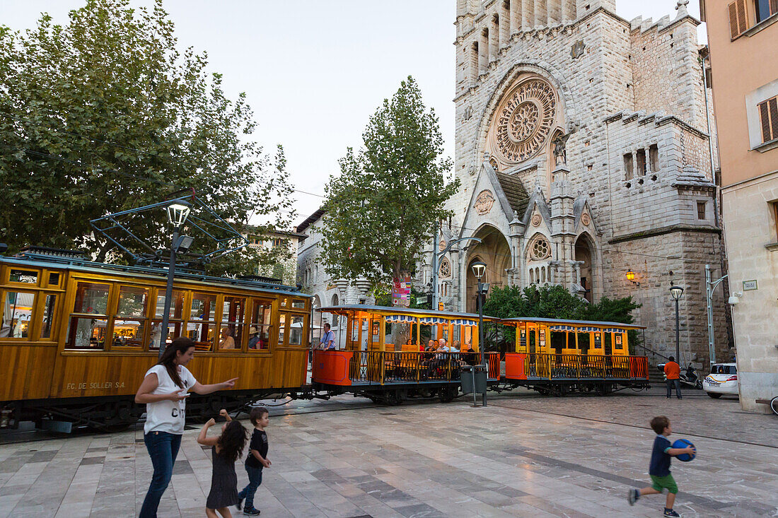 historical tram between Port de Soller and Palma de Mallorca and church of Sant Bartomeu, mother and children playing on the market square, Soller, Serra de Tramuntana, Majorca, Balearic Islands, Spain, Europe