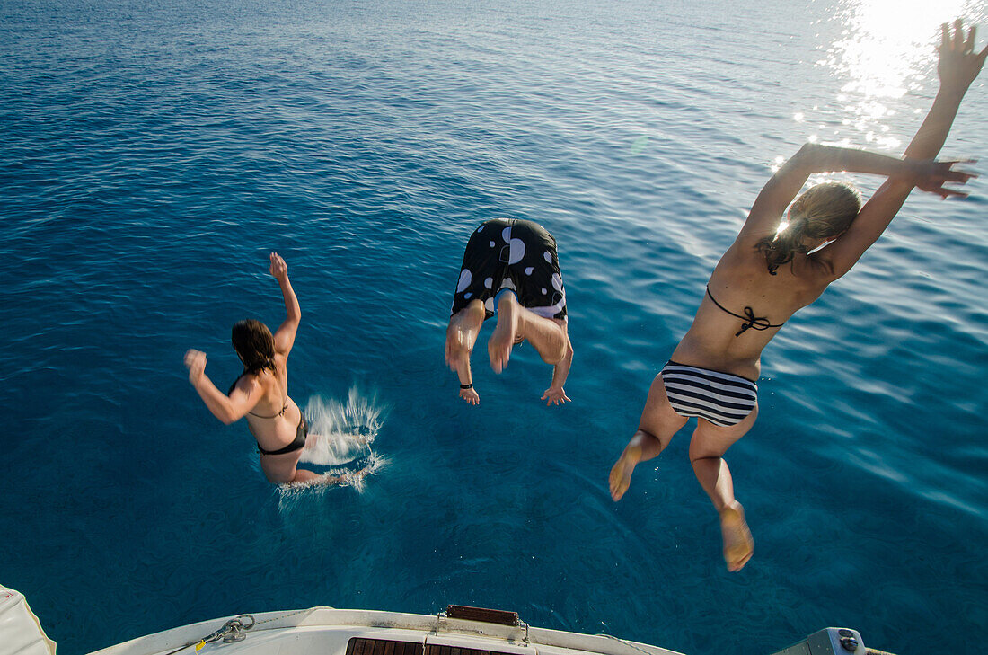 Zwei junge Frauen und ein junger Mann springen vom Heck einer Segelyacht in das klare blaue Wasser des Meeres, Mallorca, Balearen, Spanien, Europa