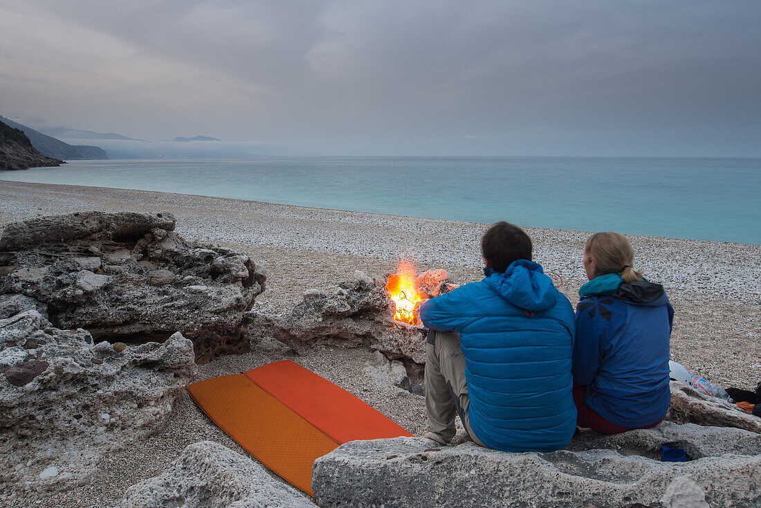 Junge Frau und Junger Mann sitzen und übernachten mit Trekkingausrüstung am Lagerfeuer am Kies-Strand der Bucht Cala Sisine, Golfo di Orosei, Selvaggio Blu, Sardinien, Italien, Europa