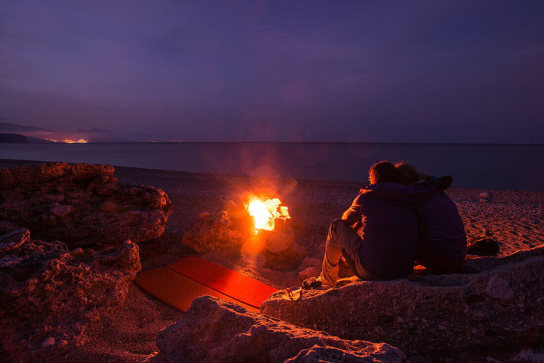 Junge Frau und Junger Mann sitzen und übernachten mit Trekkingausrüstung am Lagerfeuer am Kies-Strand der Bucht Cala Sisine, Golfo di Orosei, Selvaggio Blu, Sardinien, Italien, Europa