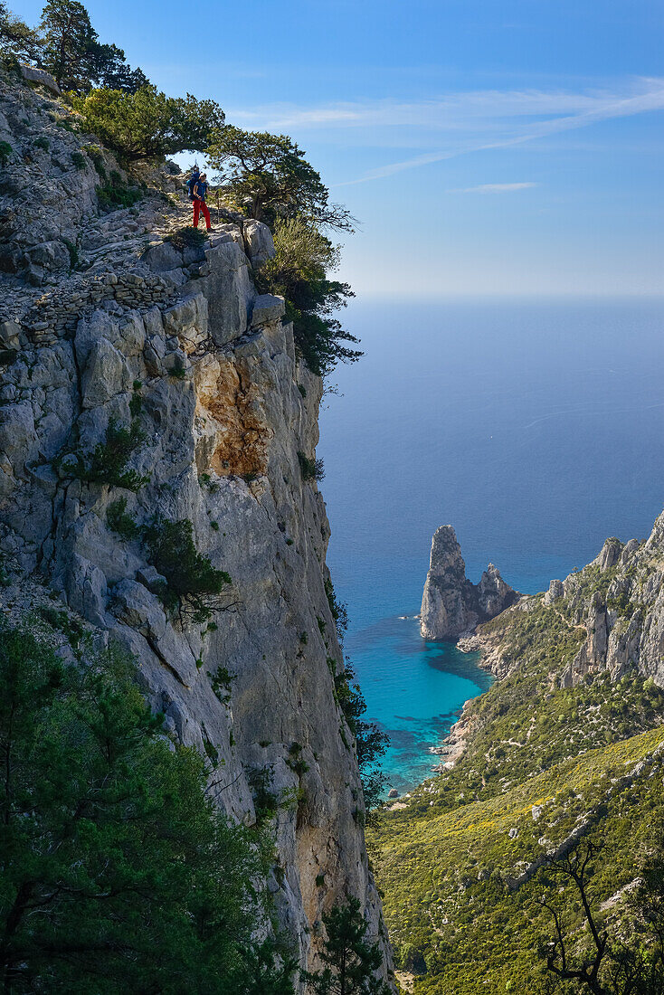 A young woman hiking along the mountainous coast, rock-needle near Pedra Longa in the background, Selvaggio Blu, Punta Giradili, Sardinia, Italy, Europe