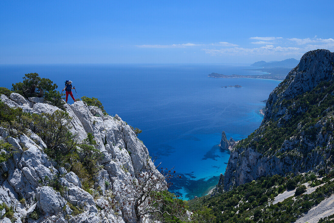 A young woman hiking along the mountainous coast, rock-needle near Pedra Longa in the background, Punta Giradili, Selvaggio Blu, Sardinia, Italy, Europe