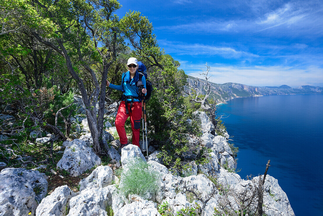 Eine junge Frau mit Trekkingausrüstung wandert oberhalb des Meeres entlang der gebirgigen Küste, Golfo di Orosei, Selvaggio Blu, Sardinien, Italien, Europa
