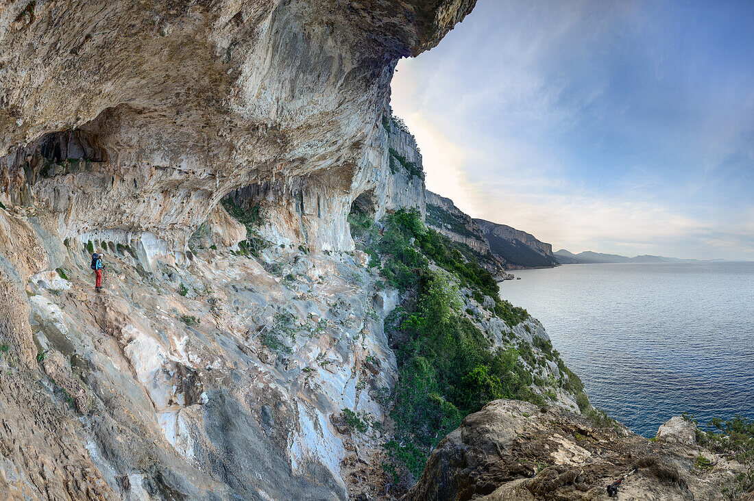 Frau mit Trekkingausrüstung steht in riesiger Höhle über dem Meer, in gebirgiger Küstenlandschaft, Golfo di Orosei, Selvaggio Blu, Sardinien, Italien, Europa