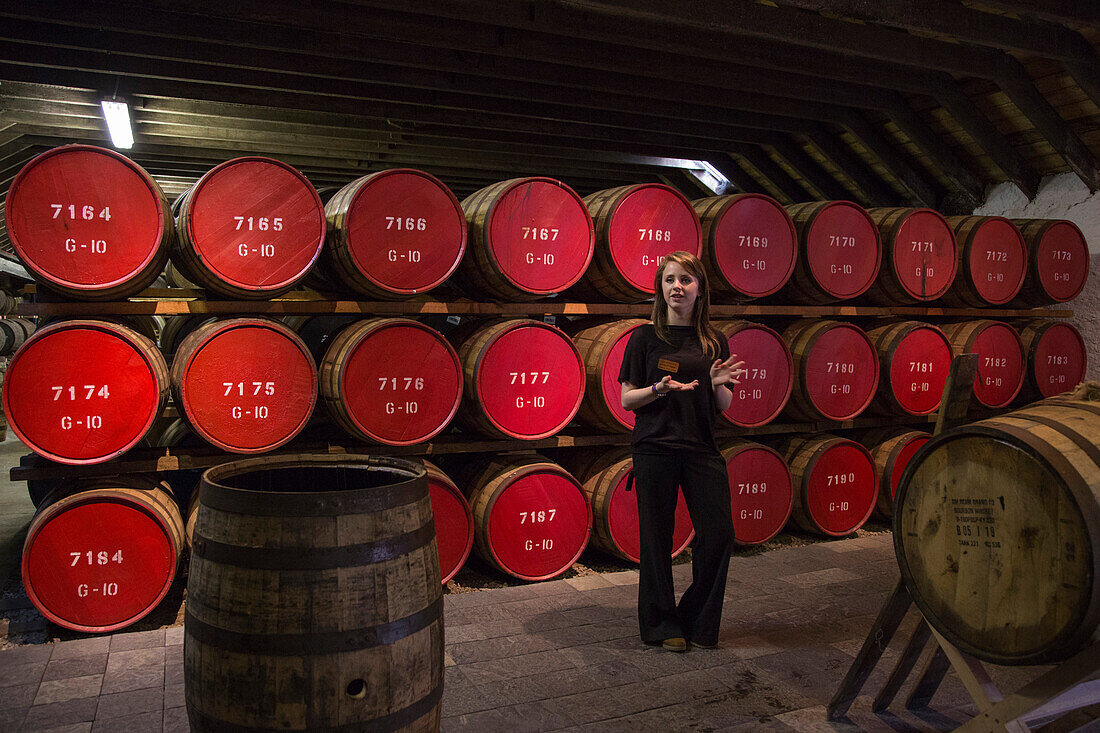 Friendly tour guide Kathryn in front of whisky ageing barrels at The Glenmorangie Whisky Distillery, Tain, Ross-shire, Highland, Scotland, United Kingdom
