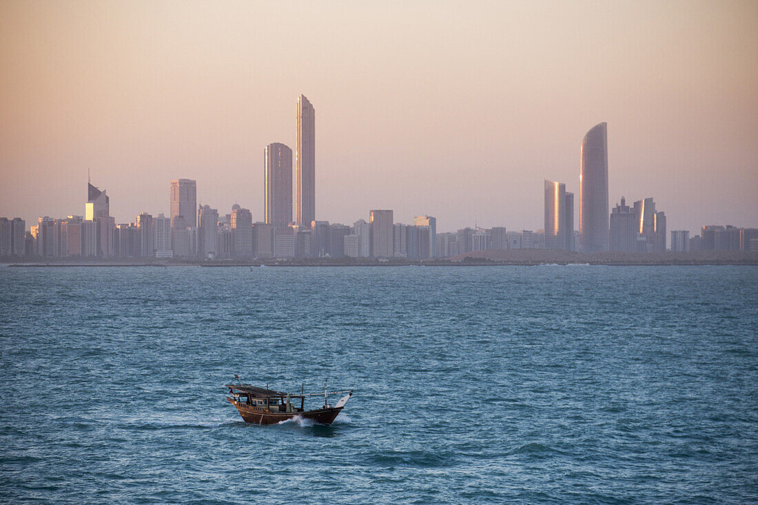 Dhow boat and city skyline at sunrise, Abu Dhabi, United Arab Emirates