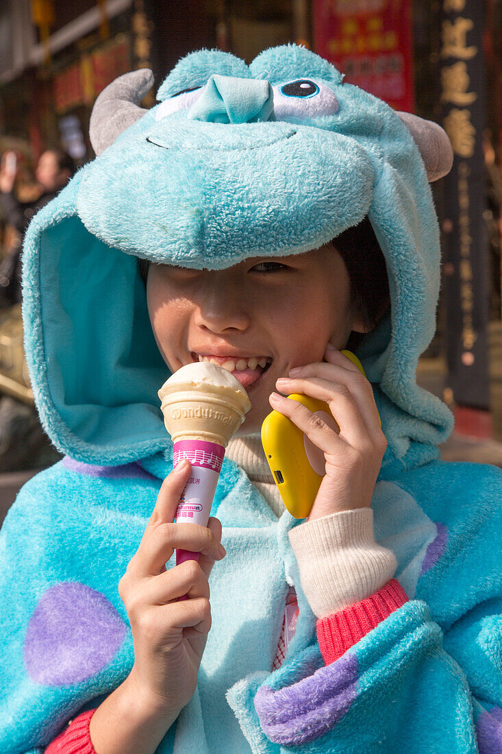 Junges Mädchen in Tierkostüm isst Eis und telefoniert mit Smartphone, Shanghai, China, Asien